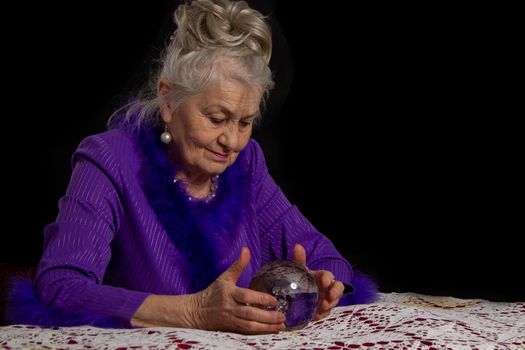 Elderly female magician with a glass ball. Fortuneteller at work.