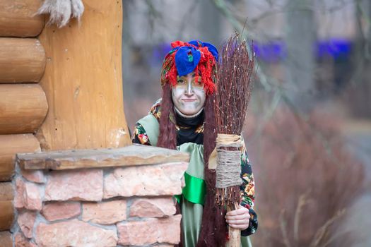 Baba Yaga with a broom near a wooden hut.