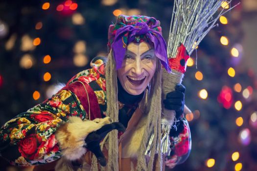 Baba Yaga with a broom on the background of the Christmas tree.