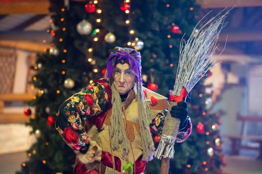 Baba Yaga with a broom on the background of the Christmas tree.
