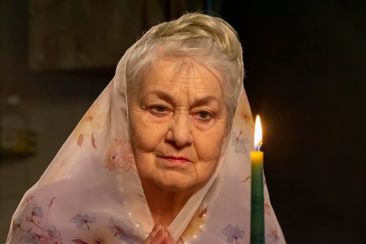 An elderly woman in a headscarf looks at a candle.An elderly woman is looking at a candle. The old woman is praying.
