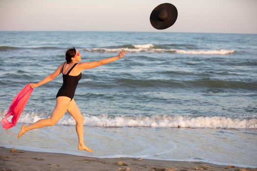 A woman runs along the shore for a hat. Holidays at sea.