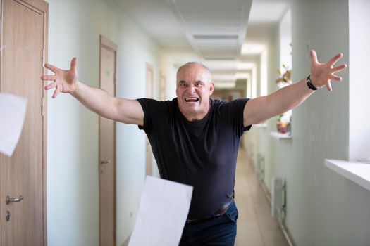A man scatters sheets. Breakdown. Stress at work. An angry man in the hallway throws paper.