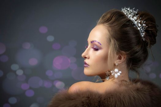 Beautiful model in profile with fashionable makeup in furs. Luxury winter girl on a gray background with bokeh.