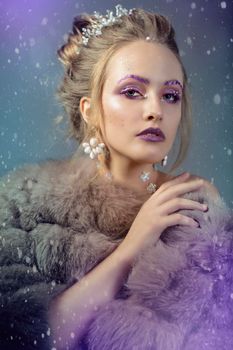 Winter girl in a fur coat in purple background. Luxurious model with beautiful makeup. Young fashionable woman.