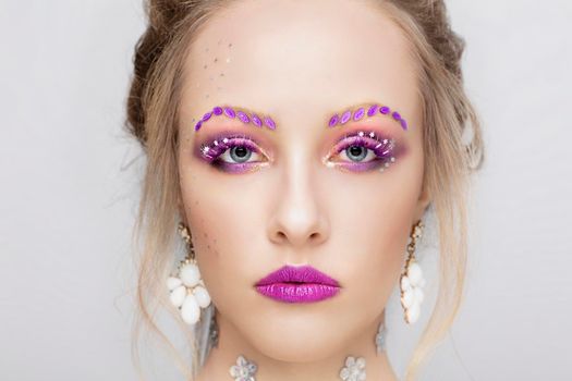 The face of a young girl. Model with purple make-up. Fancy eyebrows.Woman portrait close.