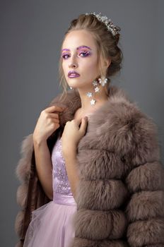 Beautiful model with fashionable make-up in a fur coat. Luxury winter girl on a gray background.