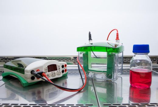 Equipment and a flask with a red liquid are placed in a glass sterile cabinet. Preparing for the experiment with the red liquid. Equipment for electrophoresis.