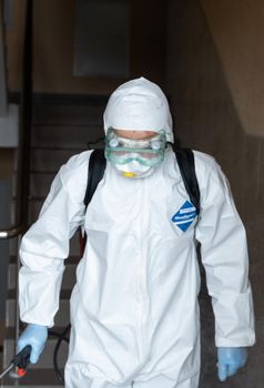UKRAINE, KYIV - May 20, 2020: Man in a white protective suit and mask is sanitizing interior surfaces inside buildings while the coronavirus epidemic for infection prevention and control of epidemic