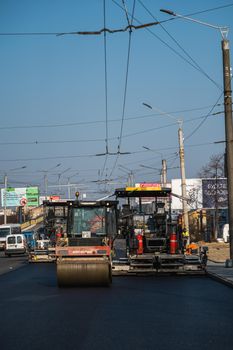 KYIV, UKRAINE - September 10, 2020: Heavy asphalt road roller with heavy vibration roller compactor that press new hot asphalt and asphalt paver machine on a road construction site on a street