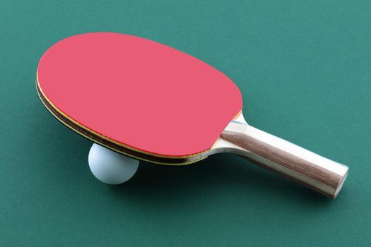 A table tennis bat and white ball on green table ping pong paddle