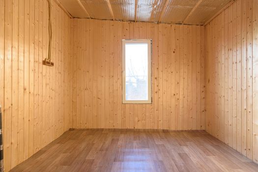 The interior of a small empty room in a country house, the walls are clapboard, linoleum is laid on the floor