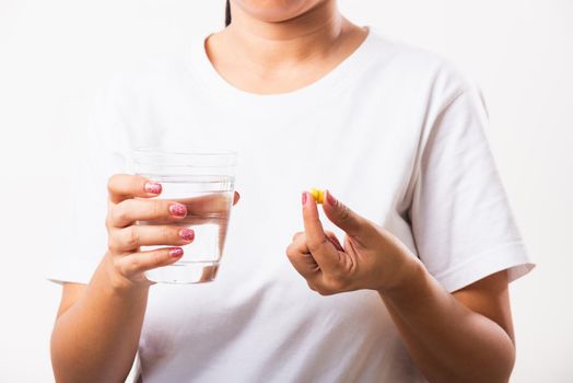 Closeup young Asian woman hold fish oil vitamin drugs in hand ready take medicines with a glass of water, studio shot isolated on white background, Healthcare and medical pharmacy concept