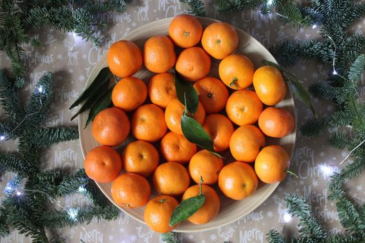 Tangerines on a plate decorated with Christmas garland and spruce branches . Christmas and new year background.