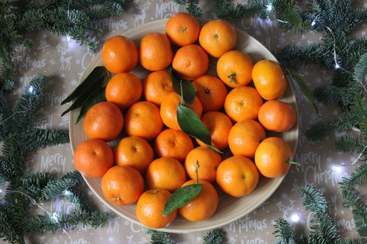 Lots of tangerines laid out on a plate and decorated with garlands and fir branches