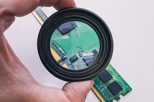 An electronics repair technician examines the faulty RAM of a computer under a magnifying glass