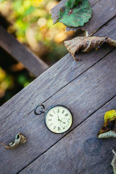 Vintage pocket watch on a wood board, colourful leaves, autumn