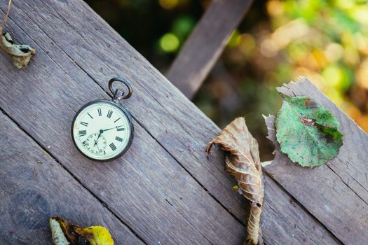 Vintage pocket watch on a wood board, colourful leaves, autumn