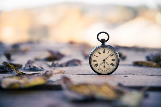 Vintage pocket watch on a wood board, colourful leaves, autumn