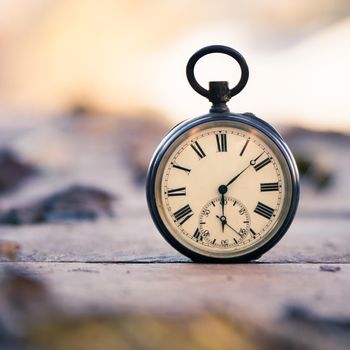 Vintage pocket watch on a wood board, colourful leaves, autumn