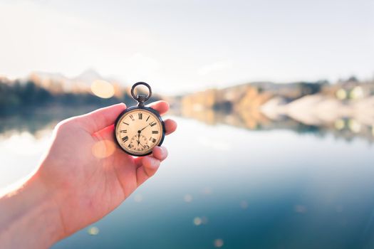 Hand held stop watch outdoors, autumn, blurry blue lake in the background