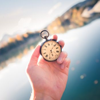 Hand held stop watch outdoors, autumn, blurry blue lake in the background