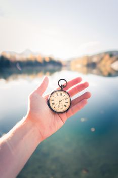 Hand held stop watch outdoors, autumn, blurry blue lake in the background