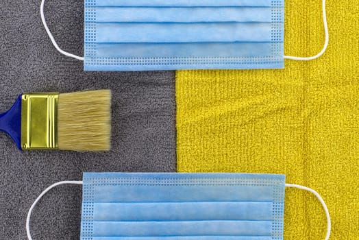 Trendy color of the year concept with clean paintbrush and protective face mask on grey - yellow textile background