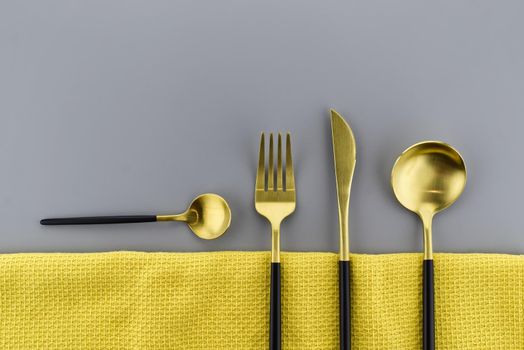 Set of stylish black and gold cutlery on a two tone grey and yellow background with copy space viewed as a flat lay. Main color trend of the year