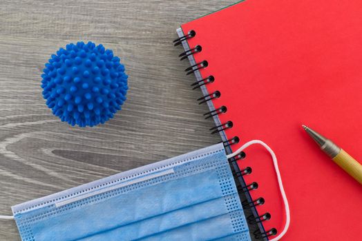Symptoms of coronavirus and medical concept with a surgical face mask with a corona virus model alongside a wire bound notepad and pen