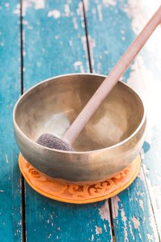 Metal singing bowl on a rustic green, wooden table outdoors.