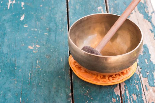 Metal singing bowl on a rustic green, wooden table outdoors.