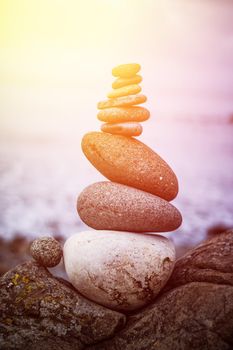 Close up picture of a stone cairn outdoors. Ocean in the blurry background. Sunshine.