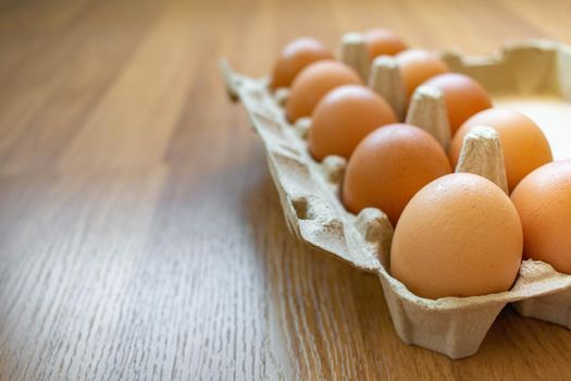 Closeup brown egg in a cardboard box from a supermarket on a wooden floor.