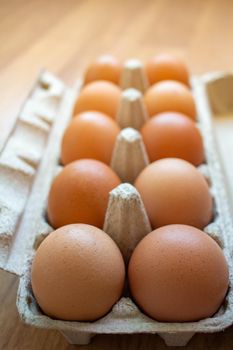 Closeup brown egg in a cardboard box from a supermarket on a wooden floor.