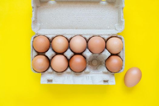 Closeup brown egg in a cardboard box from a supermarket on a yellow background.