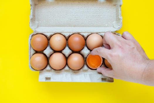 A man's hand caught a hammered brown egg. And eggs placed in paper boxes On a yellow background.