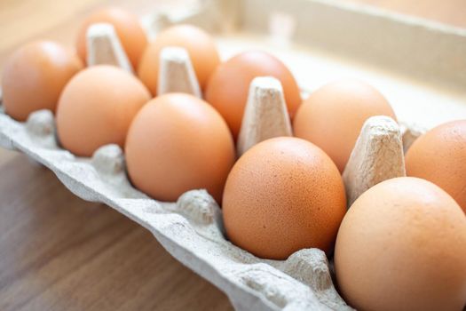 Closeup brown egg in a cardboard box from a supermarket on a wooden floor.