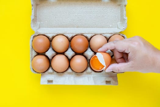 A man's hand caught a hammered brown egg. And eggs placed in paper boxes On a yellow background.