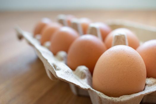 Closeup brown egg in a cardboard box from a supermarket on a wooden floor.