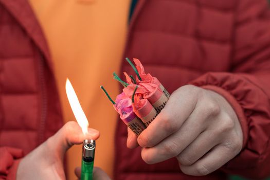 Man in Red Jacked Lighting Up Several Firecrackers in his Hand Using Gas Lighter. Guy Getting Ready for New Year Fun with Fireworks or Pyrotechnic Products