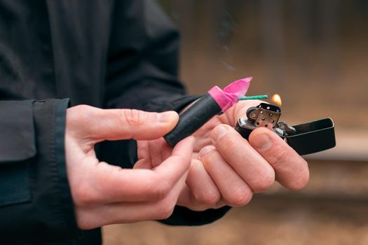 Setting Fire to the Firecracker. Man in Black Clothes Lighting Up the Petard. Firing Up the Pyrotechnics with a Black Gasoline Lighter Outdoors