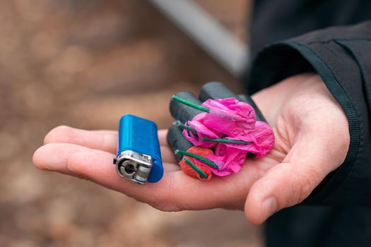 The Firecrackers in a Hand. Man Holding Five Black Petards with a Blue Gas Lighter on His Palm. A Human with a Pyrotechnics Outdoors