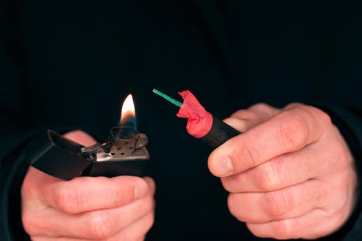 Setting Fire to the Firecracker. Man in Black Clothes Lighting Up the Petard. Firing Up the Pyrotechnics with a Black Gasoline Lighter Outdoors