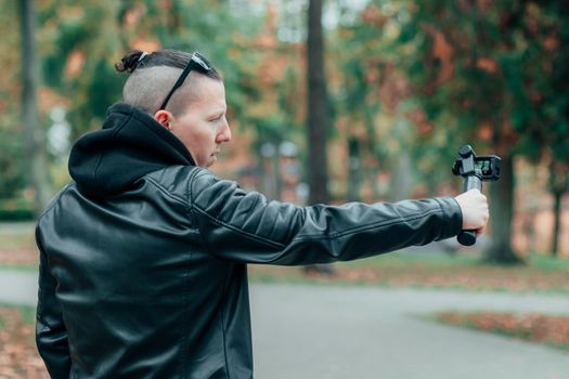 Blogger in Black Clothes and Sunglasses Making Video Using Action Camera with Gimbal Camera Stabilizer in Autumn Park