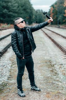 Blogger in Sunglasses Making Selfie or Streaming Video at the Pine Forest Using Action Camera with Gimbal Camera Stabilizer. Handsome Man in Black Clothes Making Photo