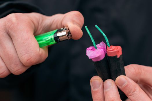 Setting Fire to the several Firecrackers. Man in Black Clothes Lighting Up Two Petards at the Same Time. Firing Up the Pyrotechnic with Green Gas Lighter Outdoors