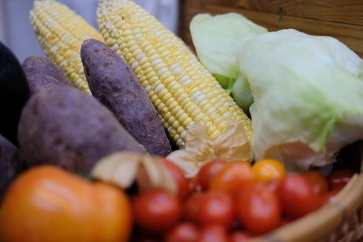 corn, purple sweet potato, tomatoes, lettuce and gooseberries in wicker basket. vegetable harvest from farm