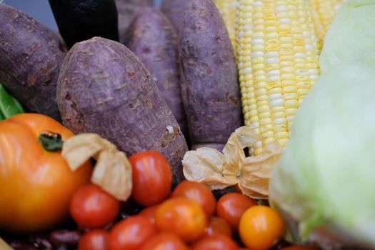 corn, purple sweet potato, tomatoes, lettuce and gooseberries in wicker basket. vegetable harvest from farm