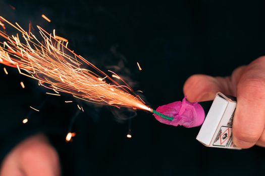 The Firecracker in a Hand. Man Holding a Burning Petard in His Hand. A Human with a Pyrotechnics that Burns with Sparks and Smoke Outdoors